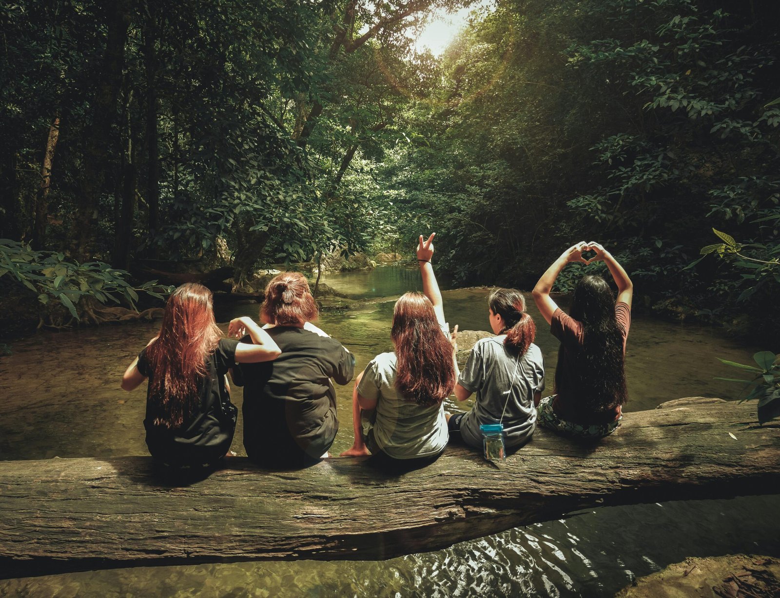 Five women enjoying nature on a log by a river in the forest, Tambon Ban Tai, Thailand.