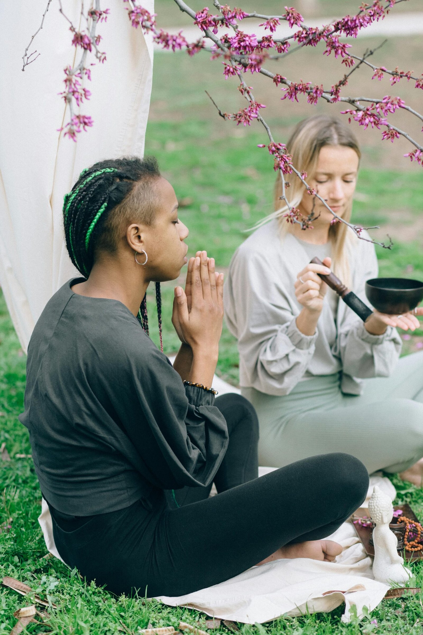 Two women meditating with singing bowl in a serene garden setting.